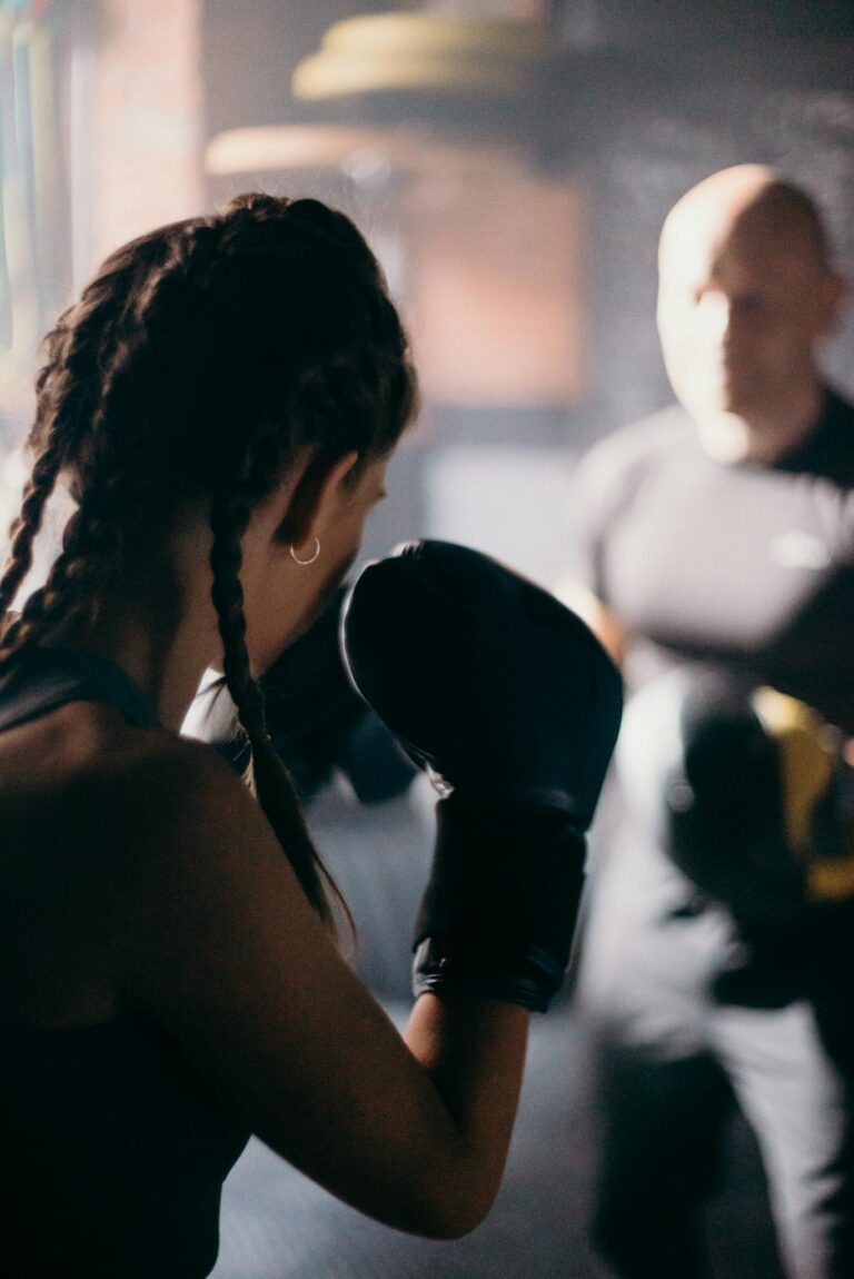 Female boxer practicing punches with a coach in a dim-lit gym.